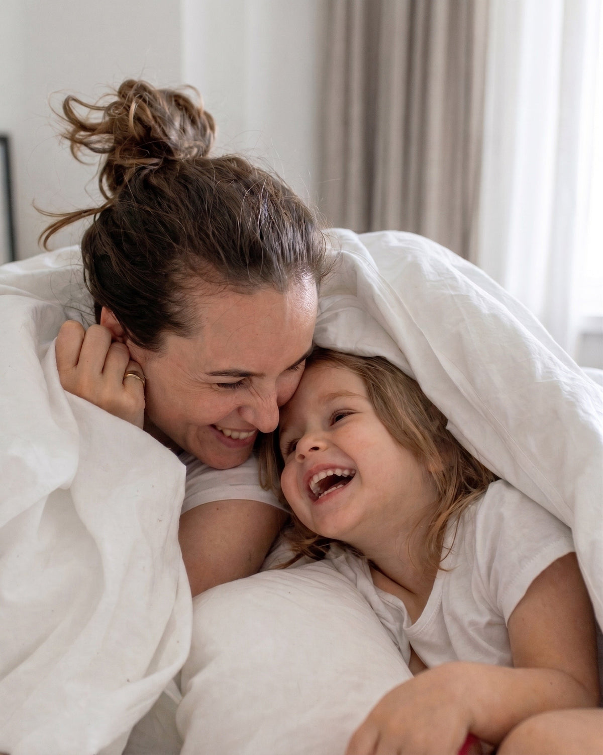 Mutter und Tochter lachen morgens unter der Decke